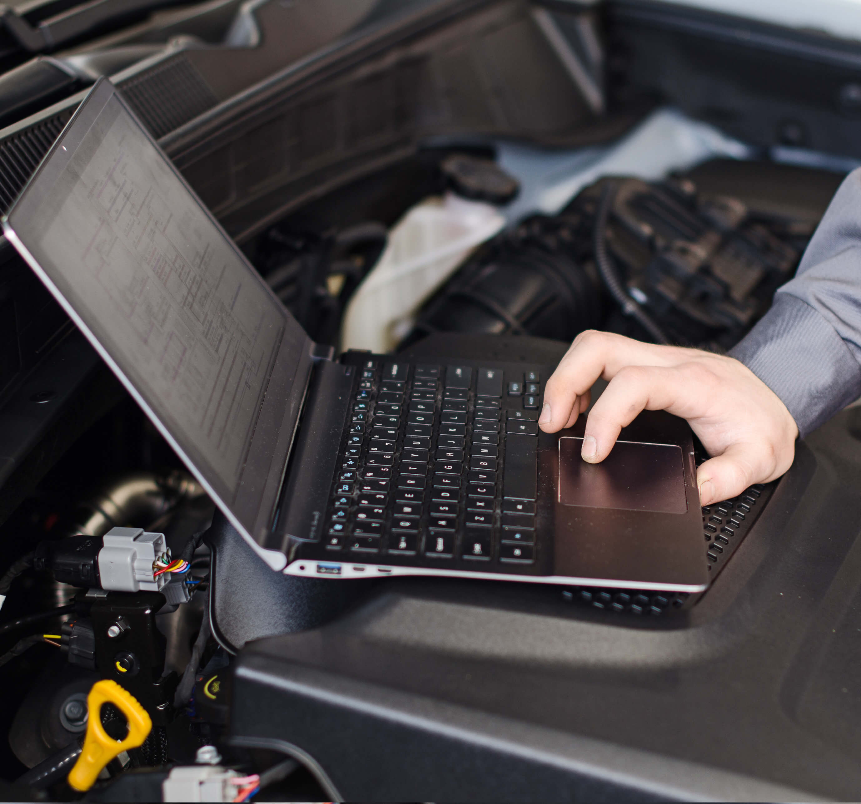 Mechanic with laptop diagnoses car in workshop.